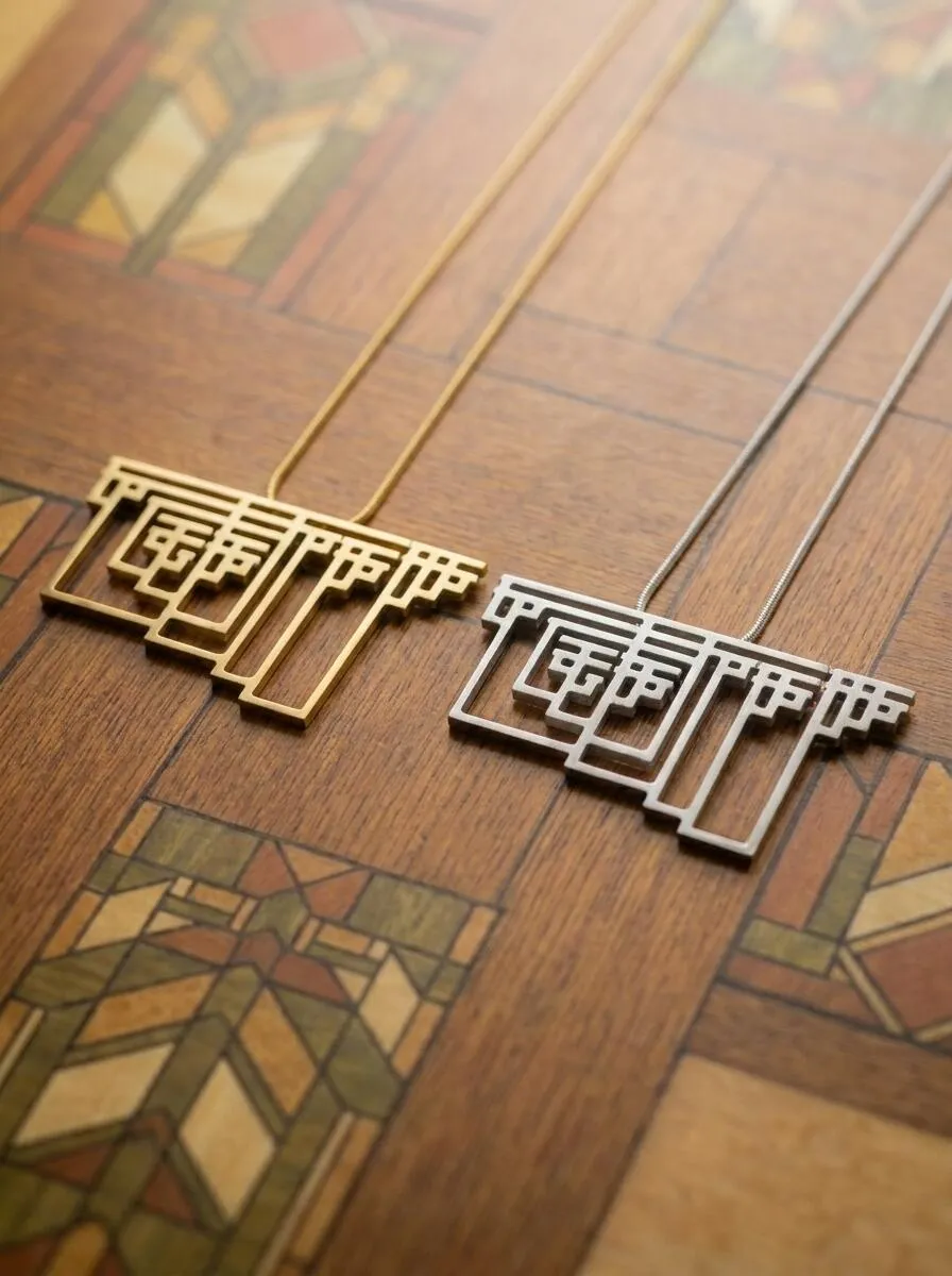 Two Graham's Necklace pendants, brass and stainless steel, against a Frank Lloyd Wright stained-glass background