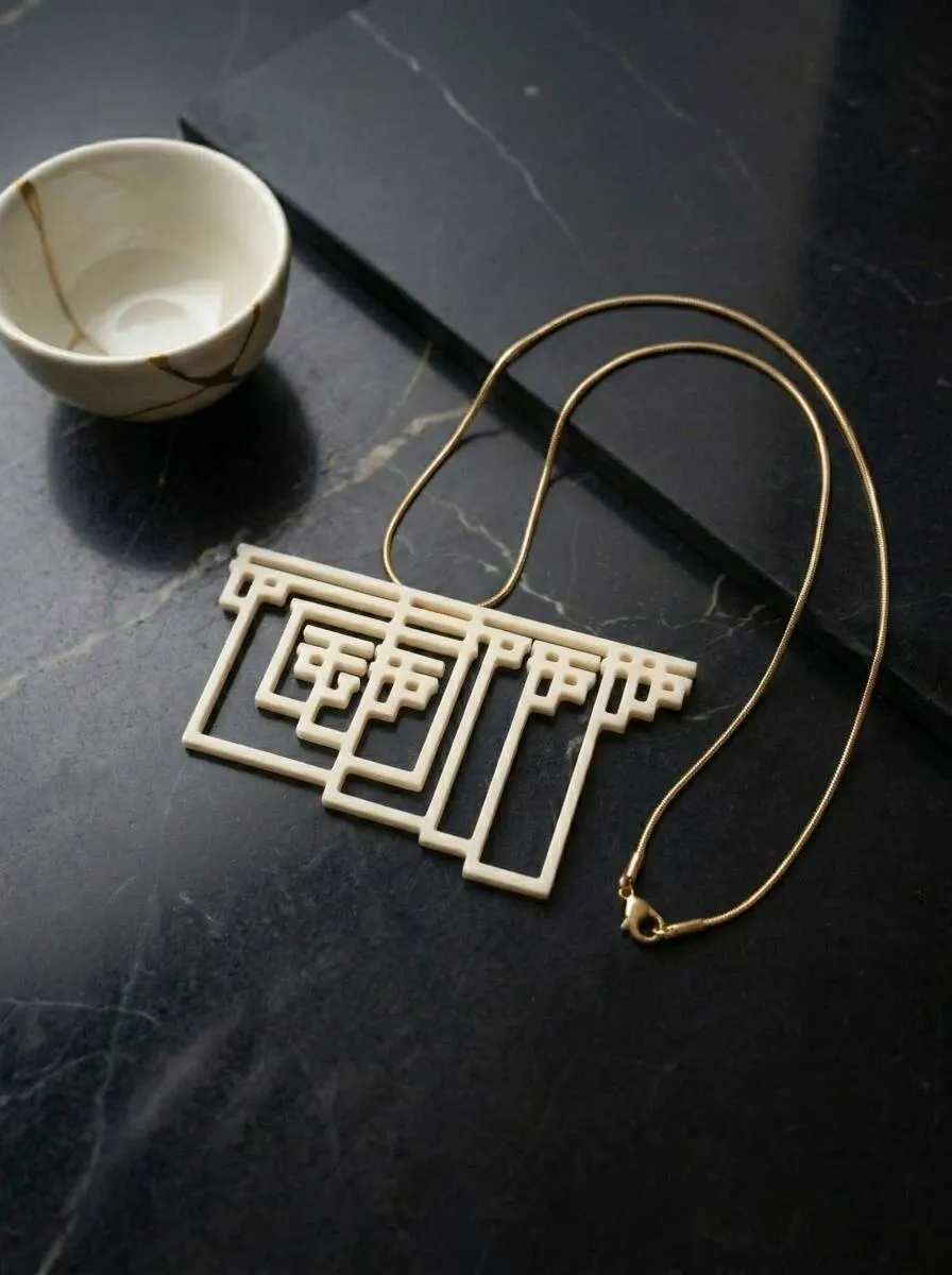 Graham's Necklace pendant in white nylon lying flat on black marble beside a small bowl