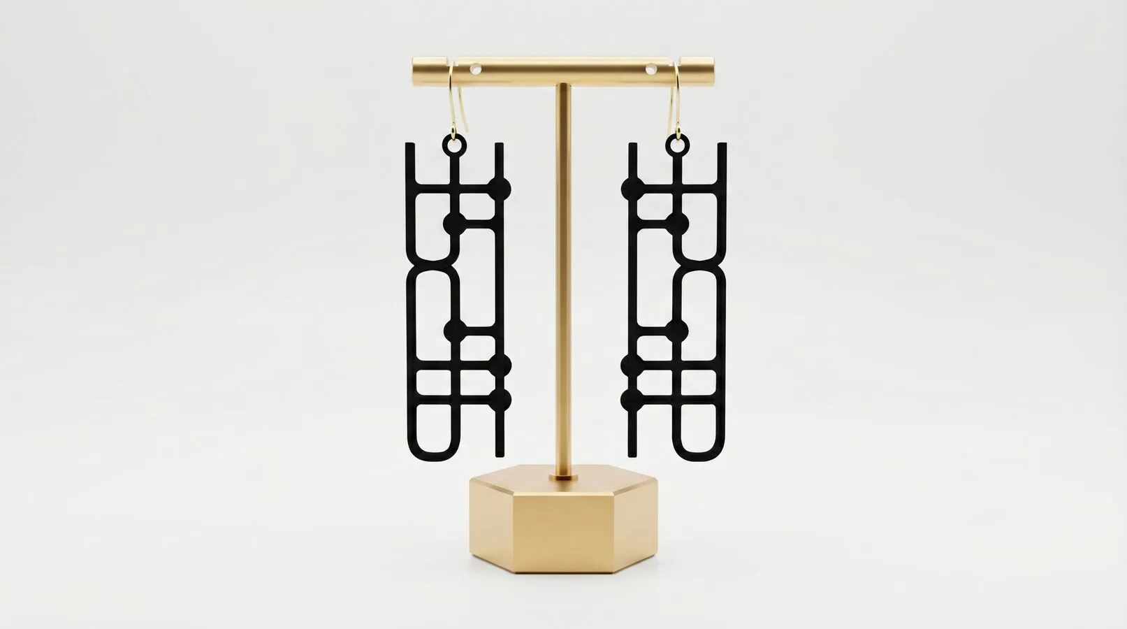 A pair of black Quantum Earrings hanging from a small brass stand