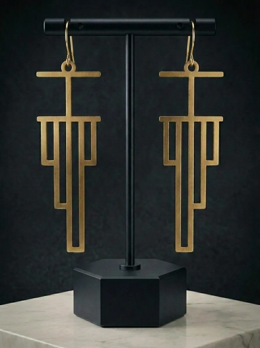 A pair of Recursion Earrings in brass hanging from a black stand